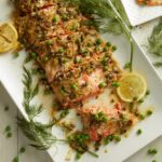 Salmon with Dill Butter Sauce and English Peas served on a white tray with herbs and lemons