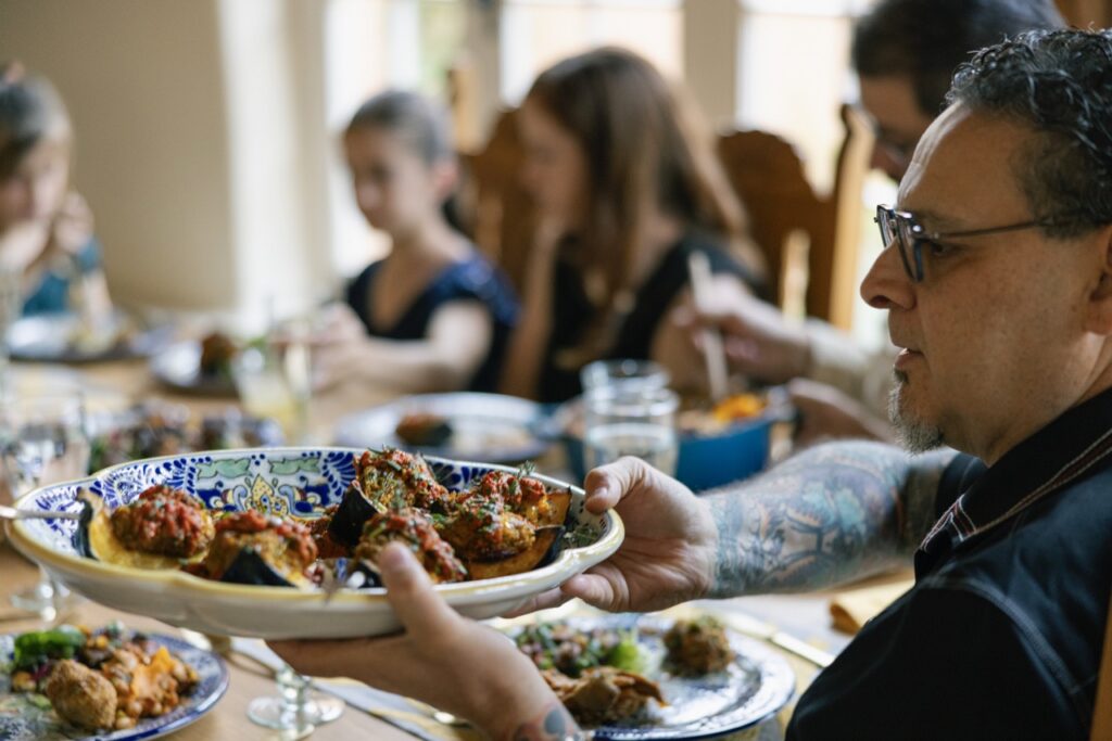 A man passes a plate of small appetizers around a dining table.