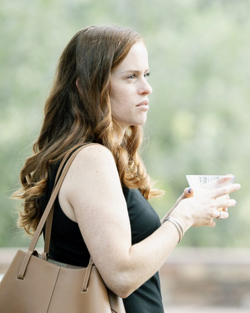 A woman stands at a profile glance, drink in hand at the Spanish colonial Art society celebration.
