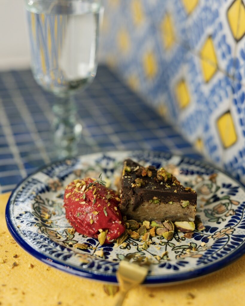 A blue pattern plate with a chocolate pistachio dessert cake and red sorbet.