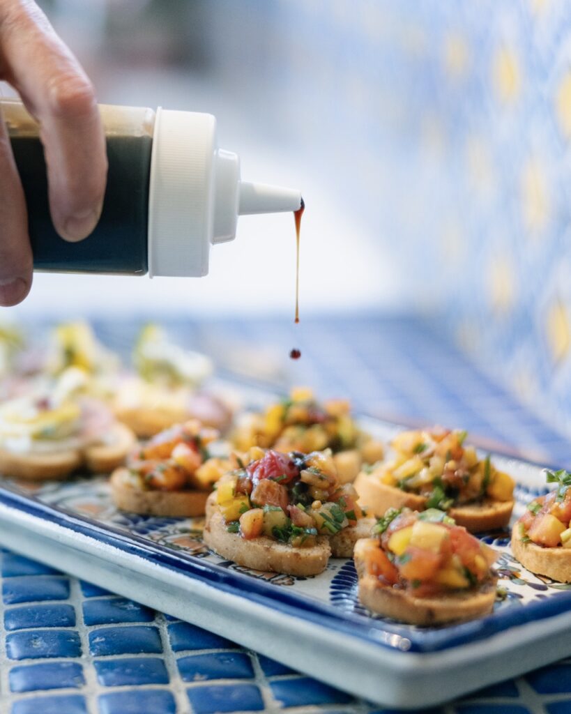 A person squeezes sauce onto small handheld appetizers at the Spanish colonial Art Society celebration.