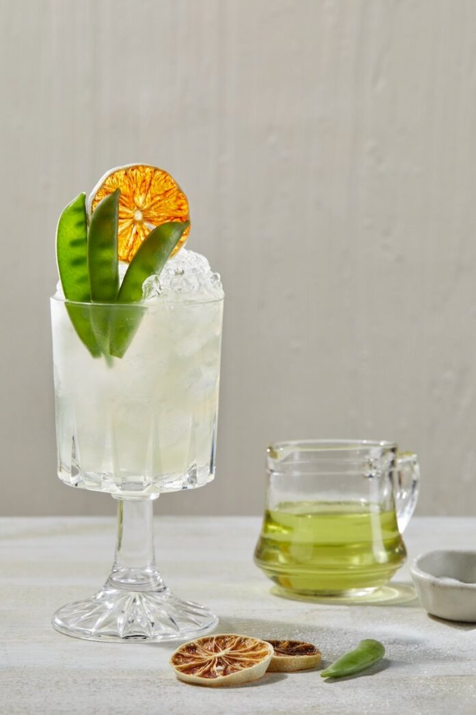 A sweet pea cocktail in a glass garnished with pea pods and an orange whel.