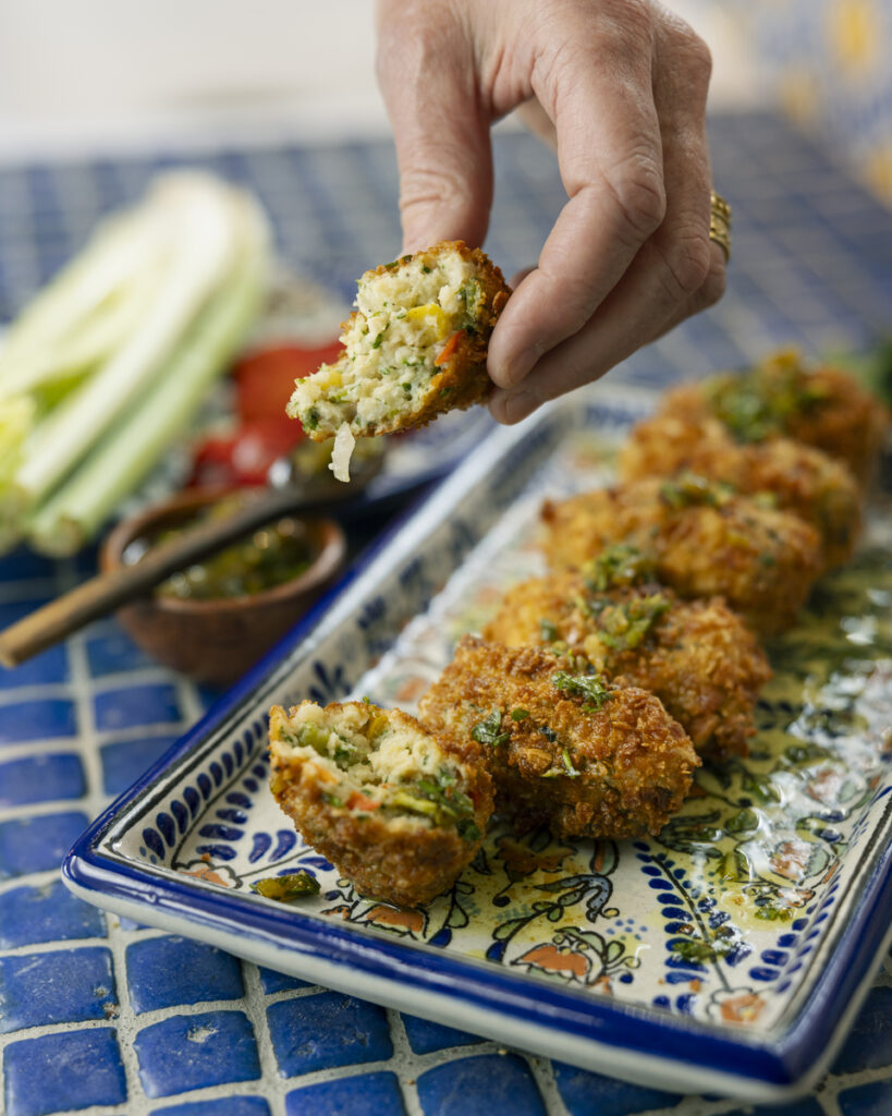 A person holds a piece of food above a plate, preparing to serve it during a multi-generational dinner of artists.
