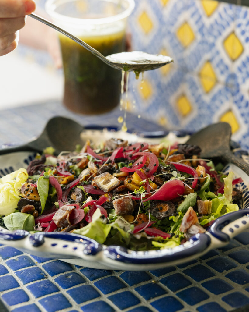 A person pours dressing over a fresh salad, enhancing its vibrant colors and textures.
