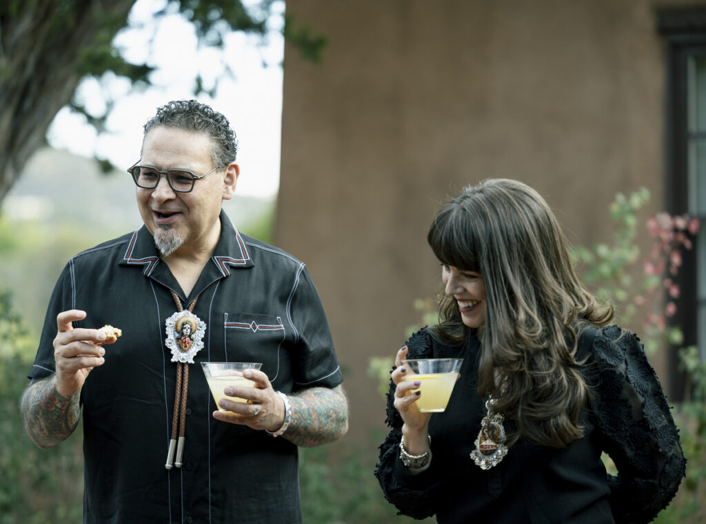 A man and woman enjoy drinks together outside, surrounded by greenery and a sunny atmosphere.