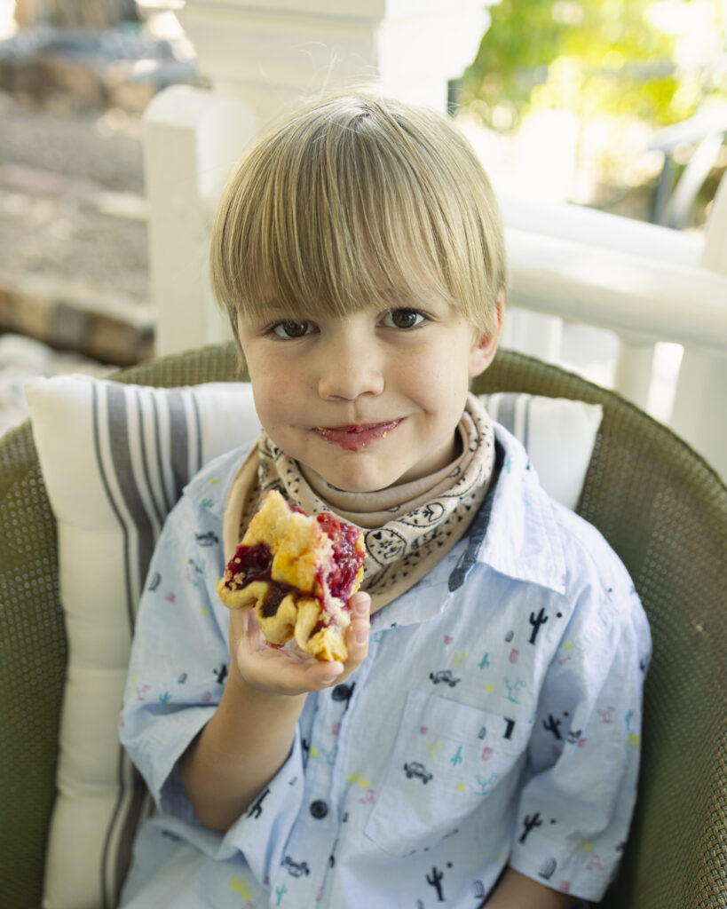 A little boy bites into a piece of cherry pie that he holds in his hand.