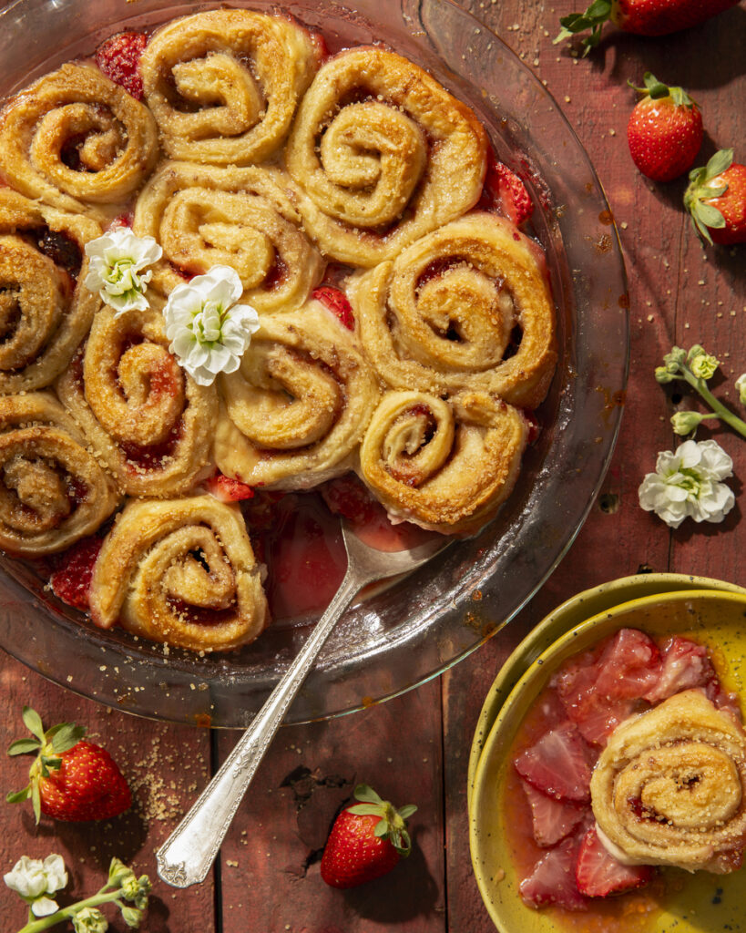A delicious pinwheel strawberry biscuit pie with fresh fruit on a dining table.