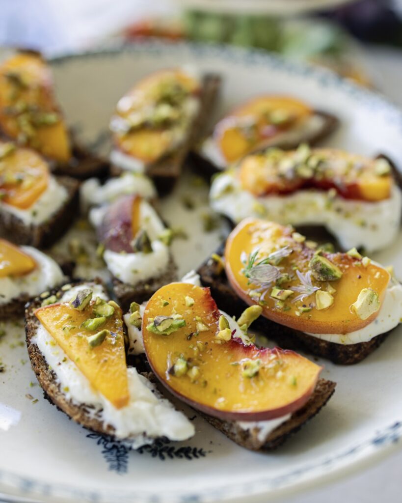 Bites of stone fruit peaches on top of goat cheese and rye bites on a white plate.