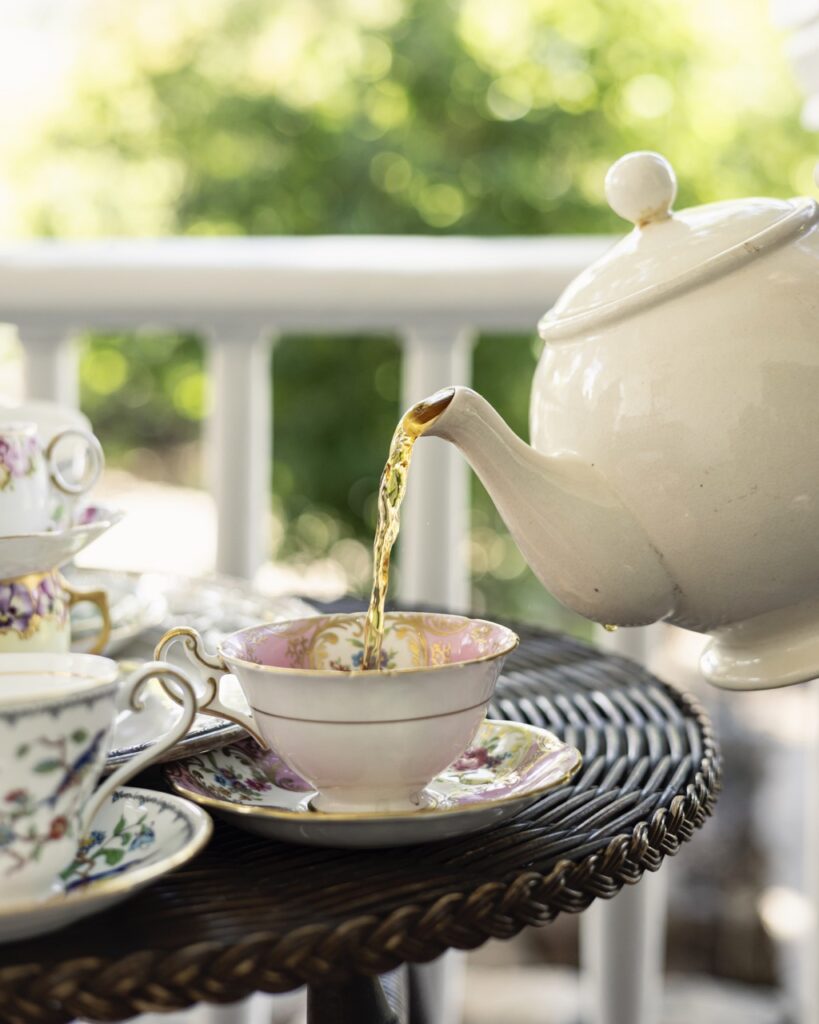 A person pours tea from a white tea pot into a white tea cup on a black wicker table at El Zaguan.