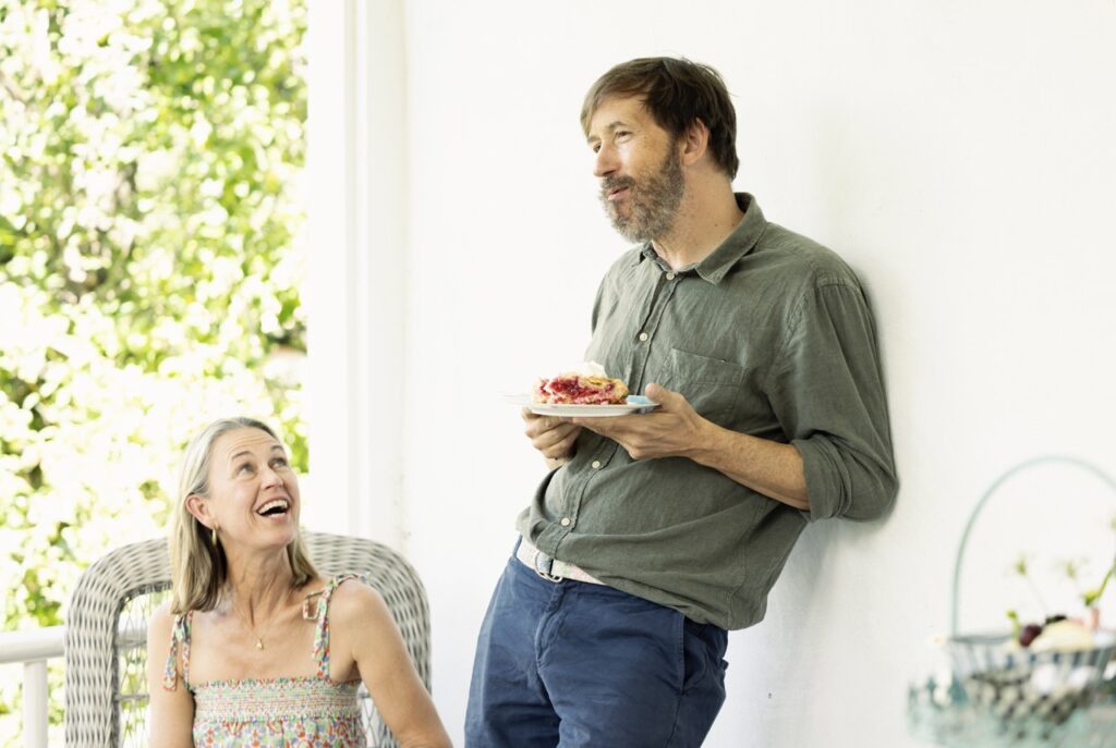 A man holds a piece of cherry pie as he leans against a white wall.