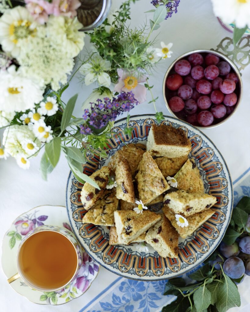 A stack of stone fruit scones sit on a plate with a bowl of honey and a bowl of stone fruit nearby.