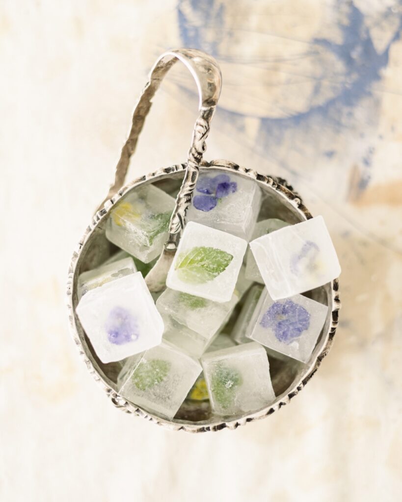 Ice cubes with little purple flowers and leaves sit in an ice bucket with a silver grabber.