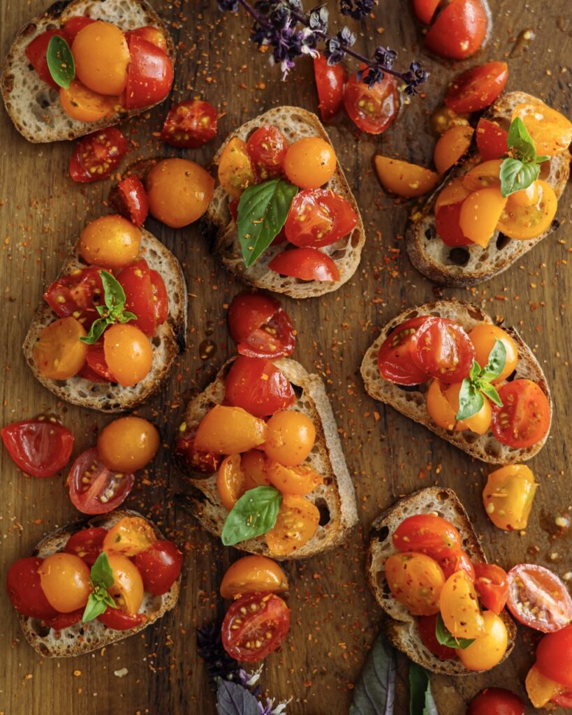 Bites of tomatoes in orange and red on pieces of bread all on a wood table.