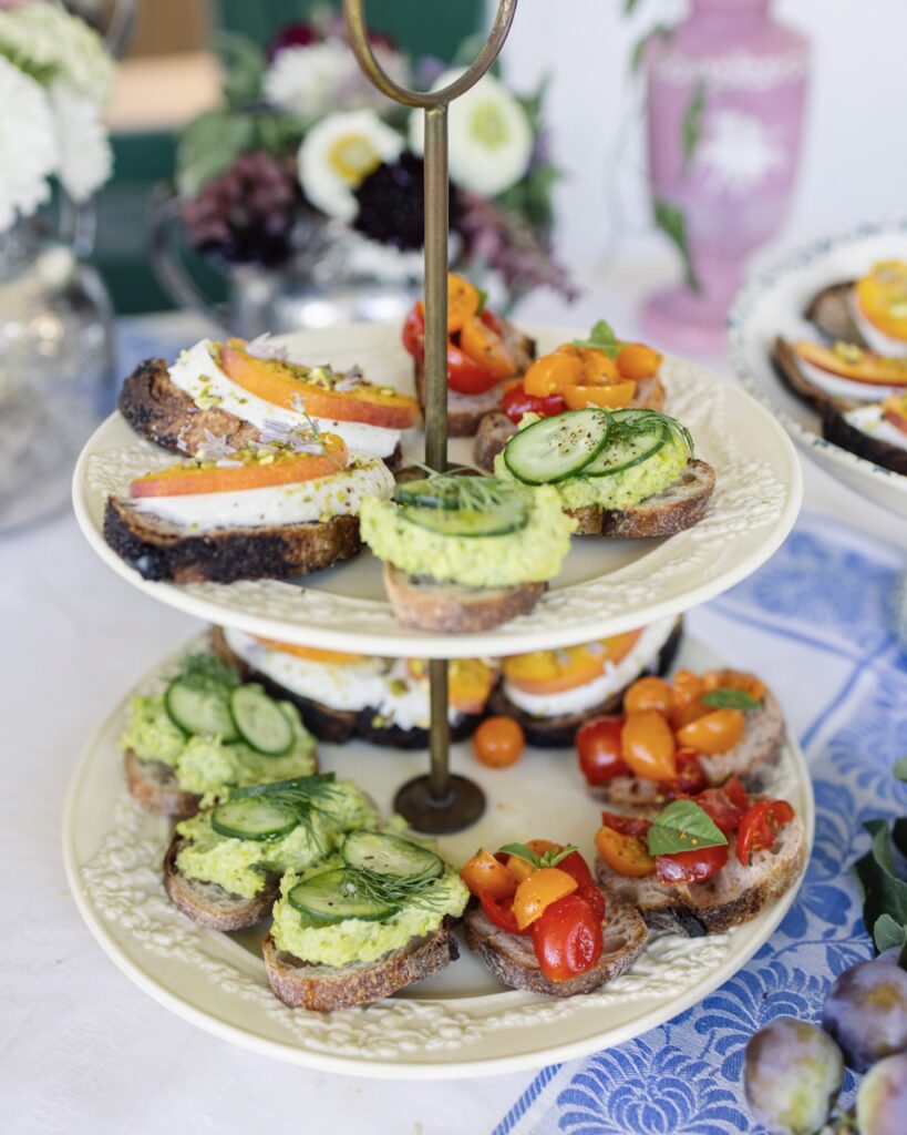 A two tier cake stand holds various stone fruit bites on white plates.