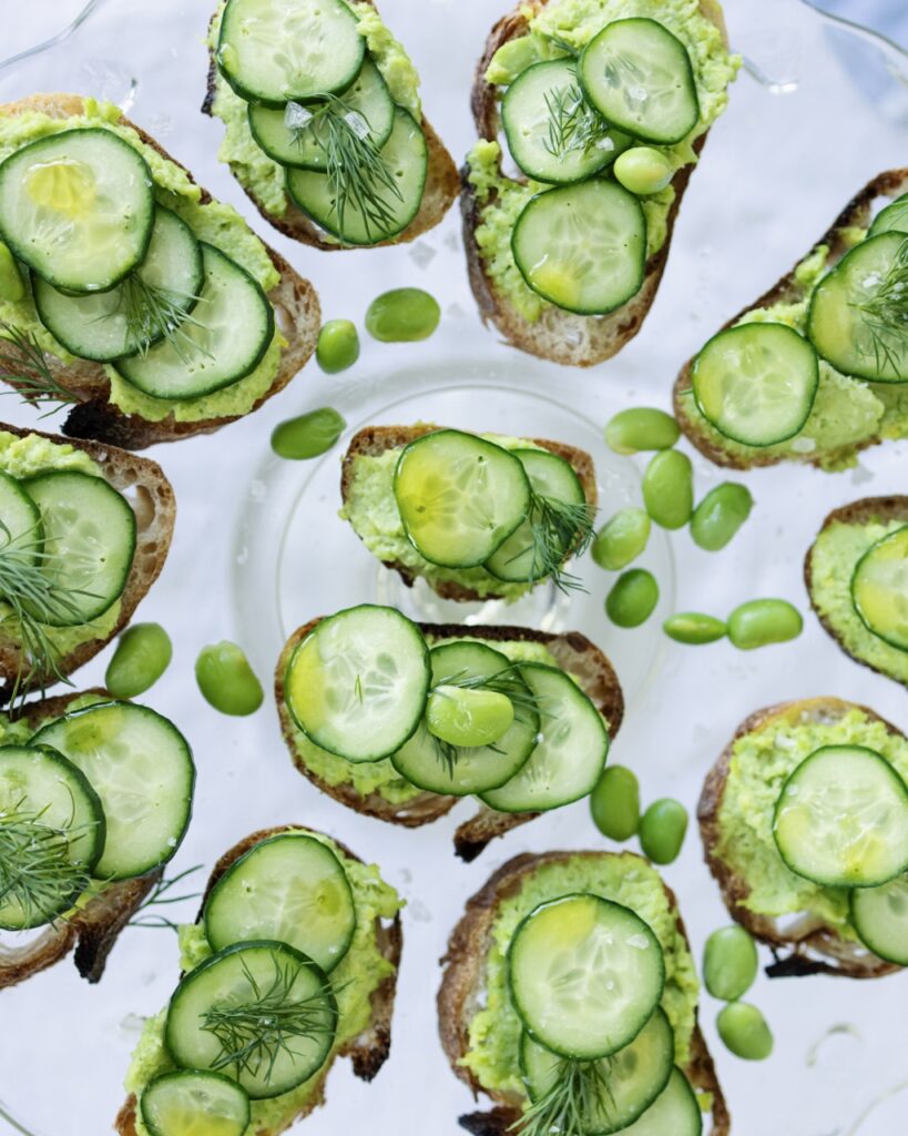 Bites of cucumber on rye bites sit arranged on a white plate.