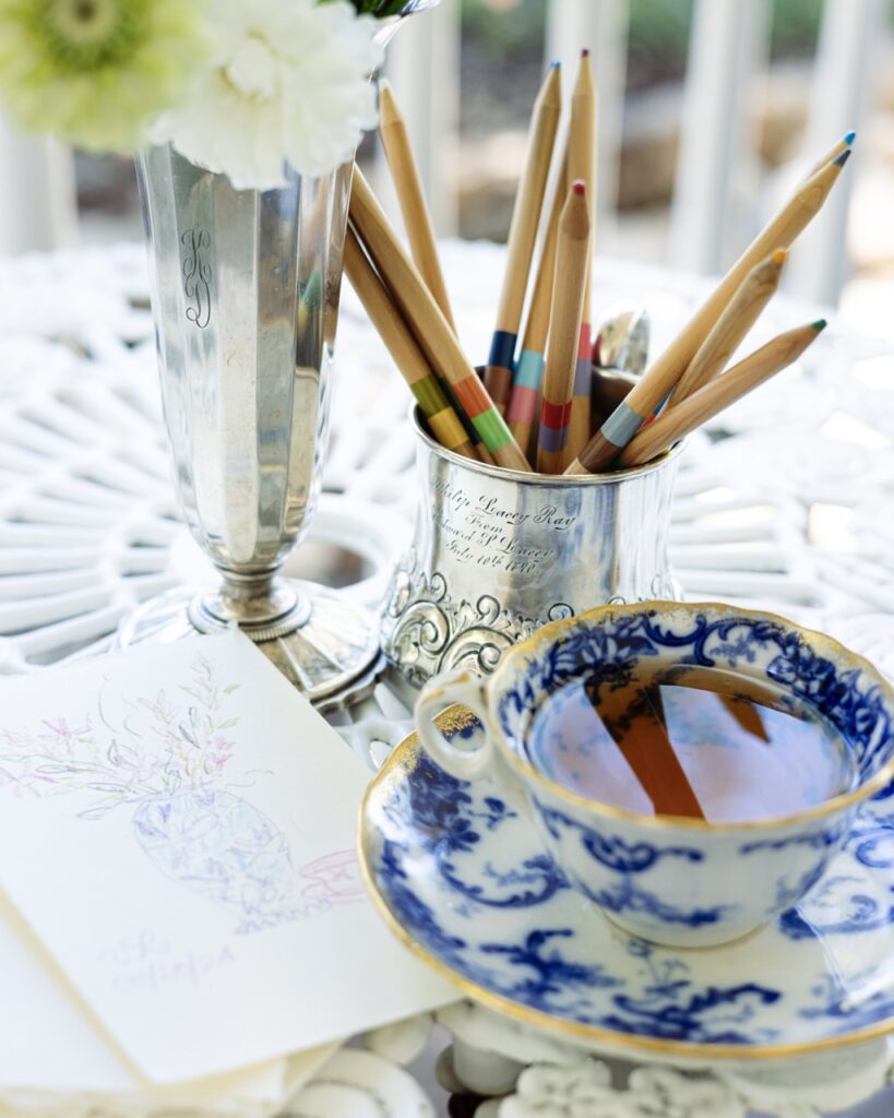 A blue and white tea cup full of tea sits beside a bucket of paint brushes.