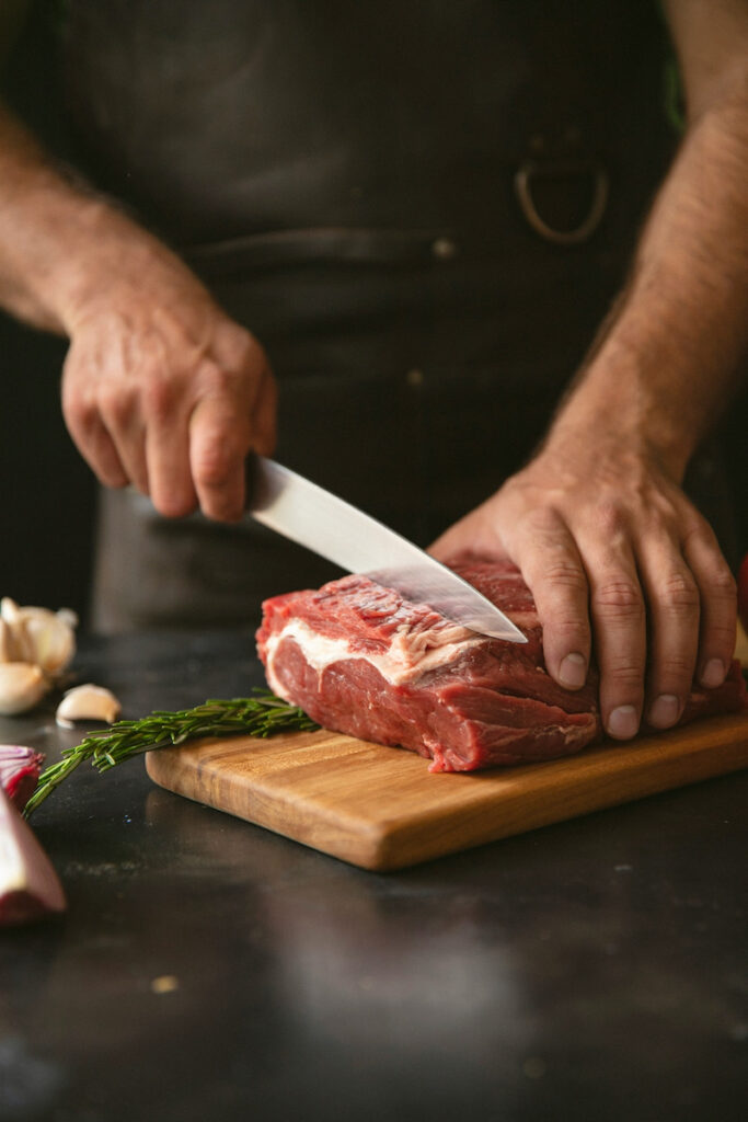 A man cuts steak with a sharp knife on a cutting board