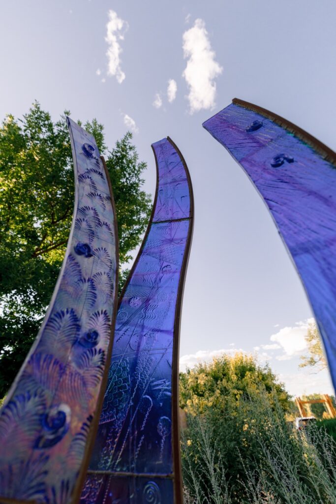 Three tall, curved, purple glass sculptures reaching towards the sky.