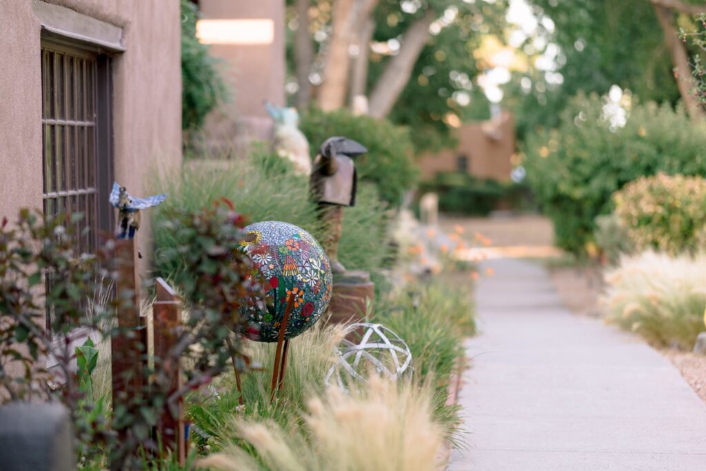 A sidewalk lined with plants and various small outdoor sculptures, including a colorful sphere.