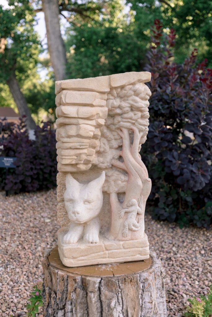 Stone sculpture of a cat-like face with a detailed tree and small figure behind it, on a wooden pedestal.