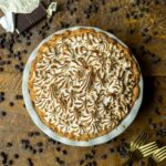 A freshly baked chocolate pudding pie with toasted meringue on top is presented on a wooden surface.