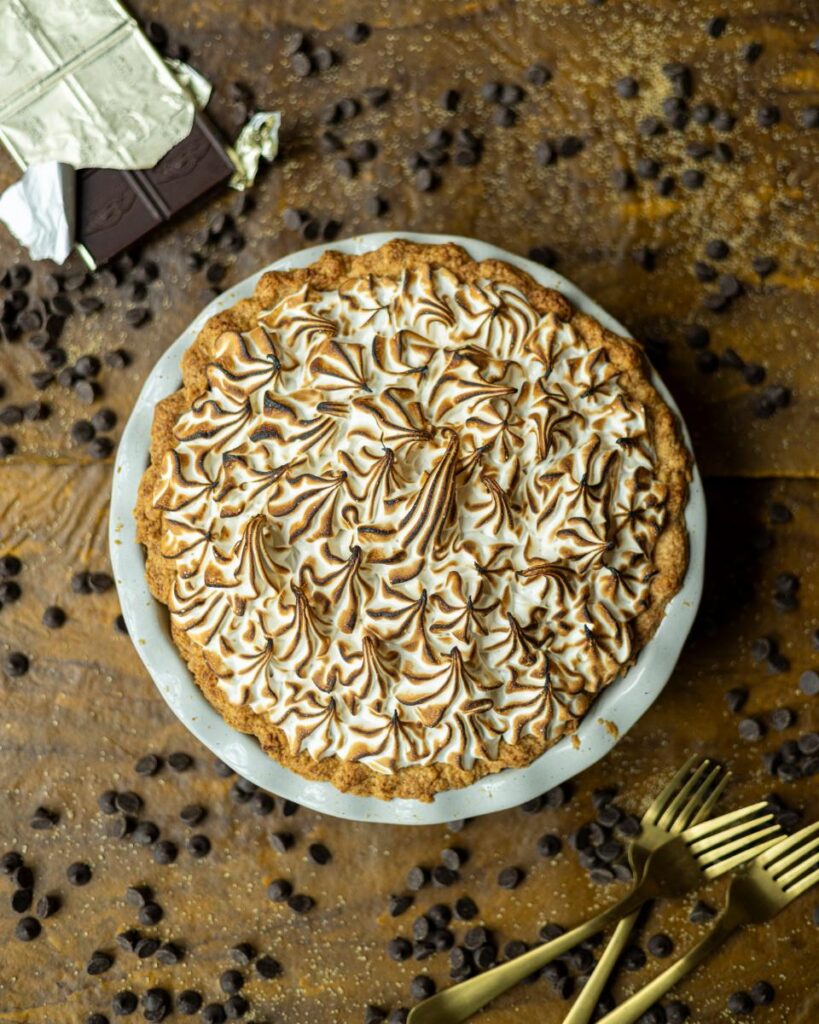 A freshly baked chocolate pudding pie with toasted meringue on top is presented on a wooden surface.