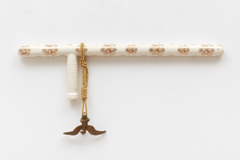 A white stick art piece with an eagle chain hanging from it.