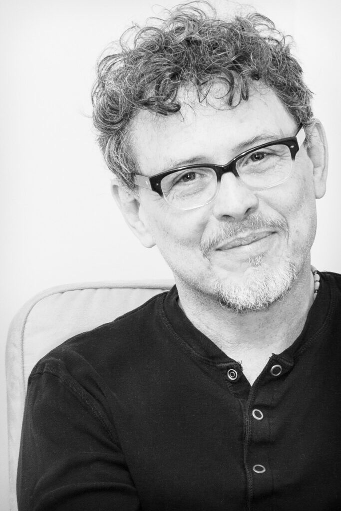 A man with glasses and a black shirt smiles to the camera.
