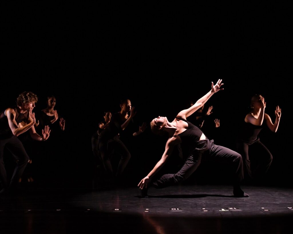 A group of Zeitgeist dancers dance under a spotlight on stage.