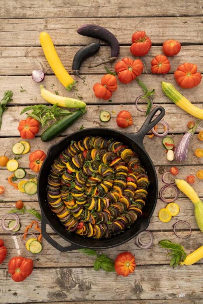 A large cast iron skillet filled with a colorful ratatouille, arranged in spirals of sliced squash and tomatoes.