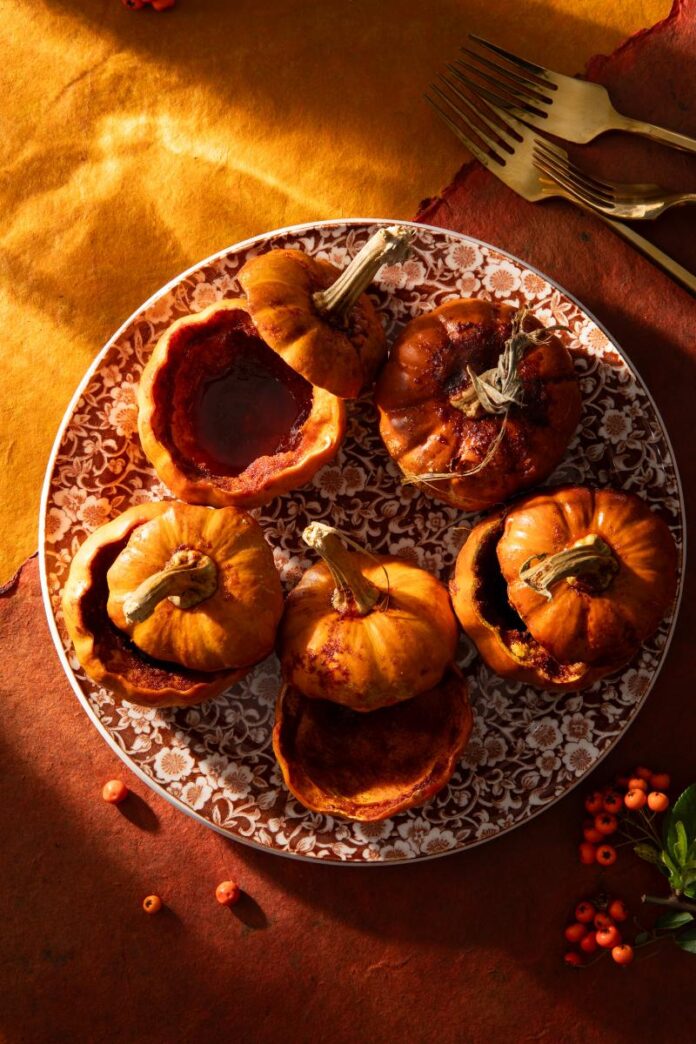 A platter holds six baked baby pumpkins, some with their tops removed and filled with a sauce.