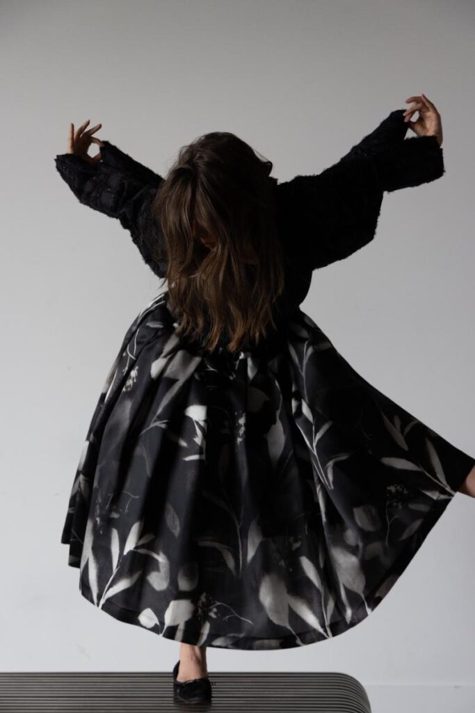 A model wearing a black and silver silk skirt with an abstract print and a black textural jacket with a rear zipper.