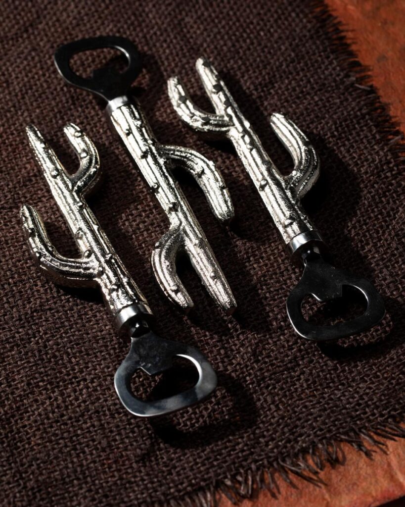 
Three metallic, cactus-shaped bottle openers are laid on a brown burlap surface.