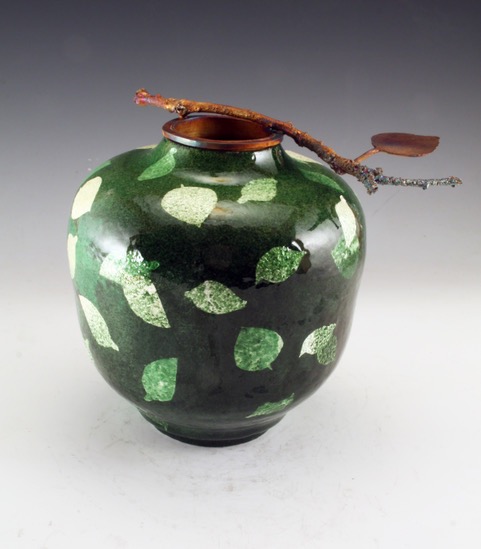 A pottery vase with leaves and a branch coming out of the top.