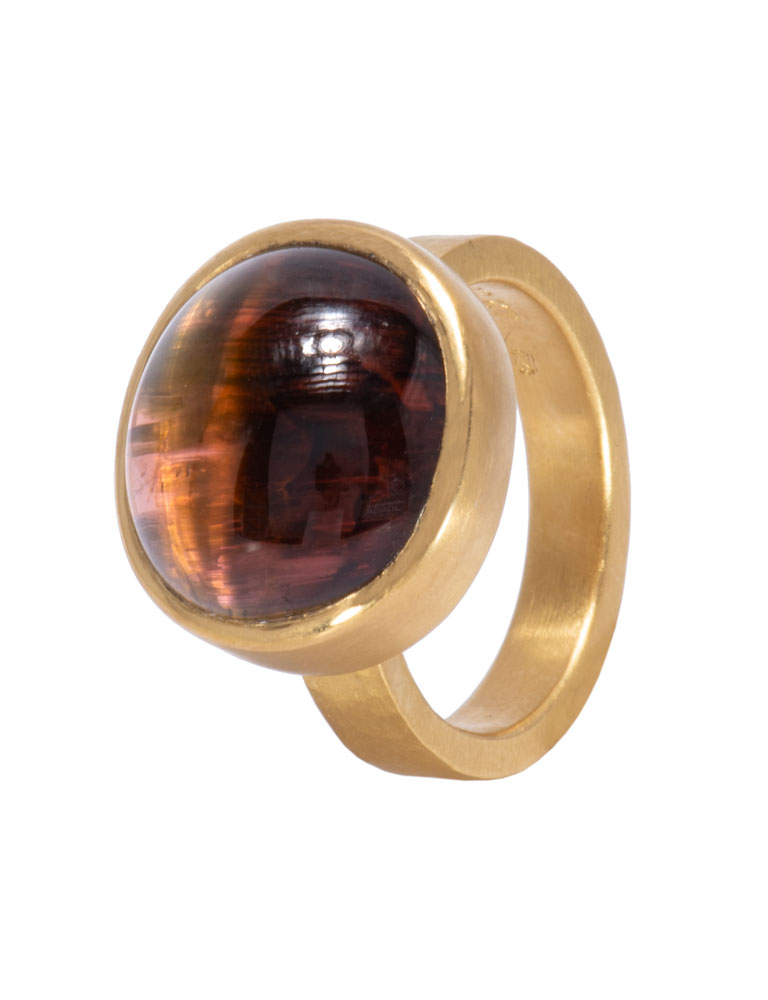 A gold ring with a large, round, reddish-brown gemstone that has a thin white line of light running through it.