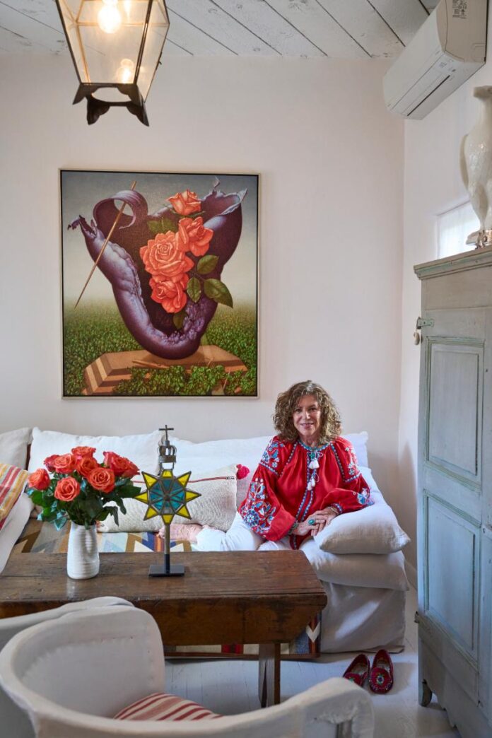 A woman with long, curly brown hair, wearing a vibrant red tunic with intricate white and blue embroidery on the sleeves.