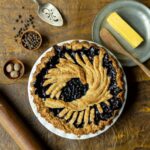 A dark purple huckleberry-merlot pie with a decorative woven crust is on a white plate.