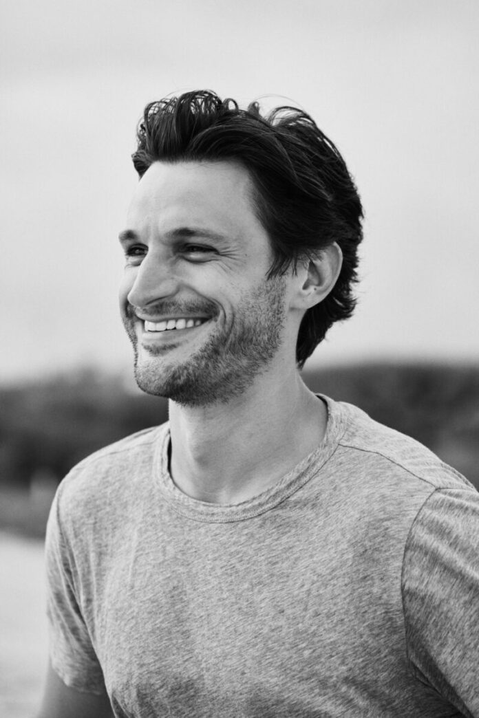 A black and white headshot of a man outside in a t shirt.