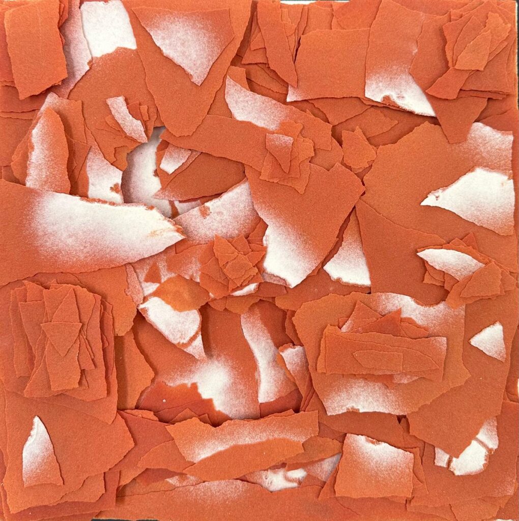 An abstract mixed-media piece made of ripped, layered pieces of orange paper with scattered white spray paint on them.