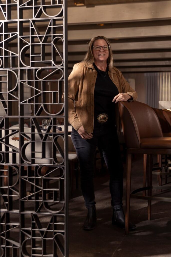 Kathleen Crook is smiling while standing in a restaurant.
