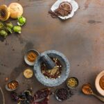 A flat lay photo showing ingredients for Mexican mole sauce, including various chiles, nuts, spices, and a stone mortar and pestle on a rustic metal surface.