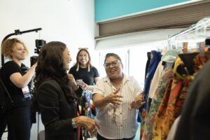 Native Fashion Week 2025 13 TABLE Magazine A woman in a striped shirt shows another woman a clothing rack.