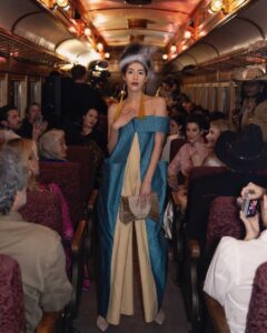 Native Fashion Week 2025 27 TABLE Magazine A woman in blue and gold dress poses in the bus aisle.