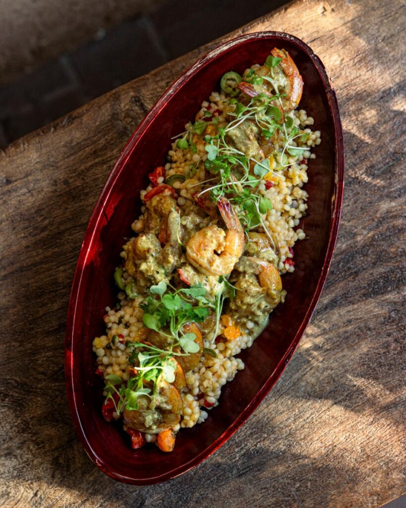An overhead close-up shot of a dark red, oblong serving platter filled with a bed of Israeli couscous.