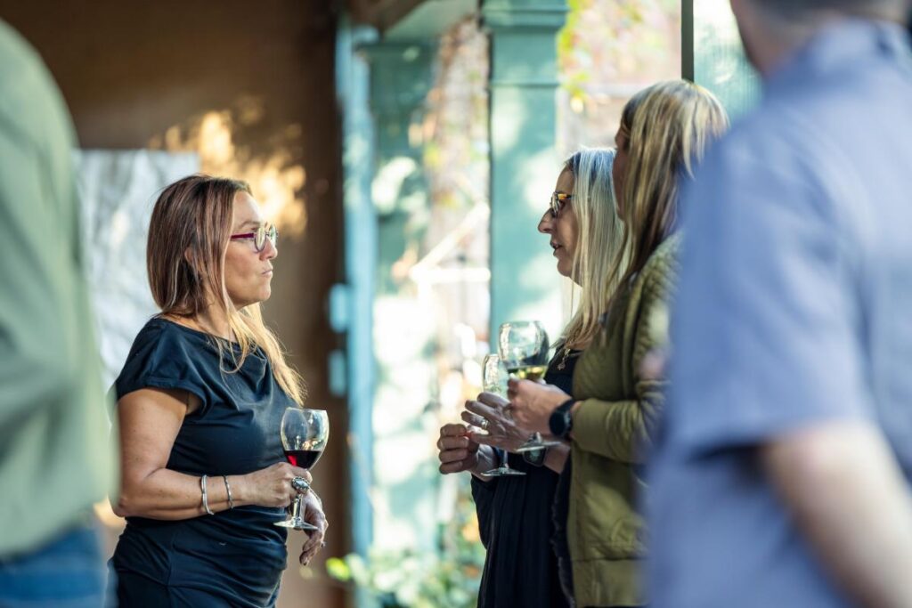 A group of people standing and talking with wine glasses in hand in an art gallery.