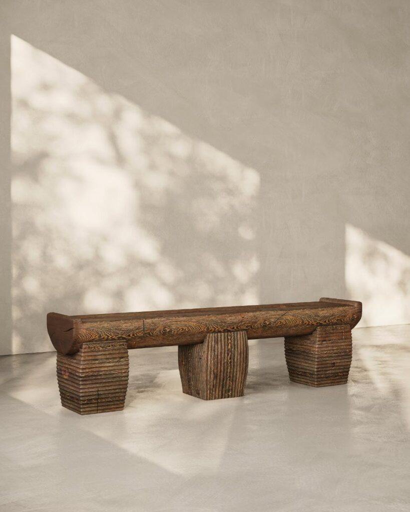 A large wooden bench with a cylindrical center support and two rectangular end supports sits in a sunlit room.