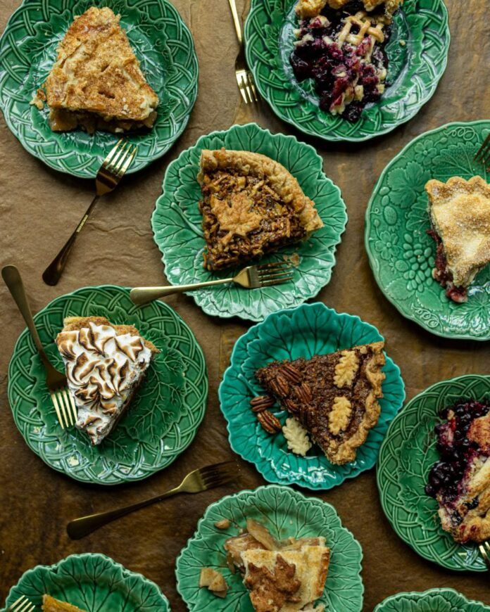 A top-down view of six slices of different pies arranged on green, leaf-shaped plates with gold forks.