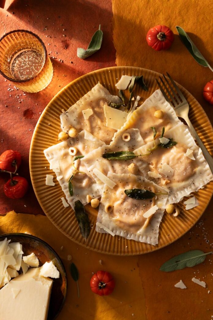 A plate of pumpkin-stuffed ravioli is garnished with brown butter, sage, hazelnuts, and shaved cheese.