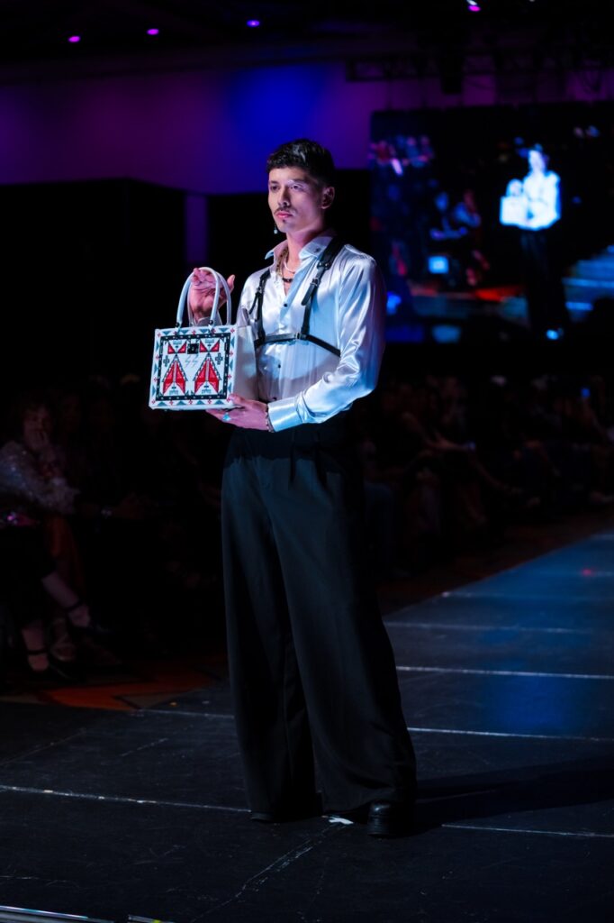 SWAIA Native Fashion Week 4 TABLE Magazine A man in a white shirt displays a white and red bag.