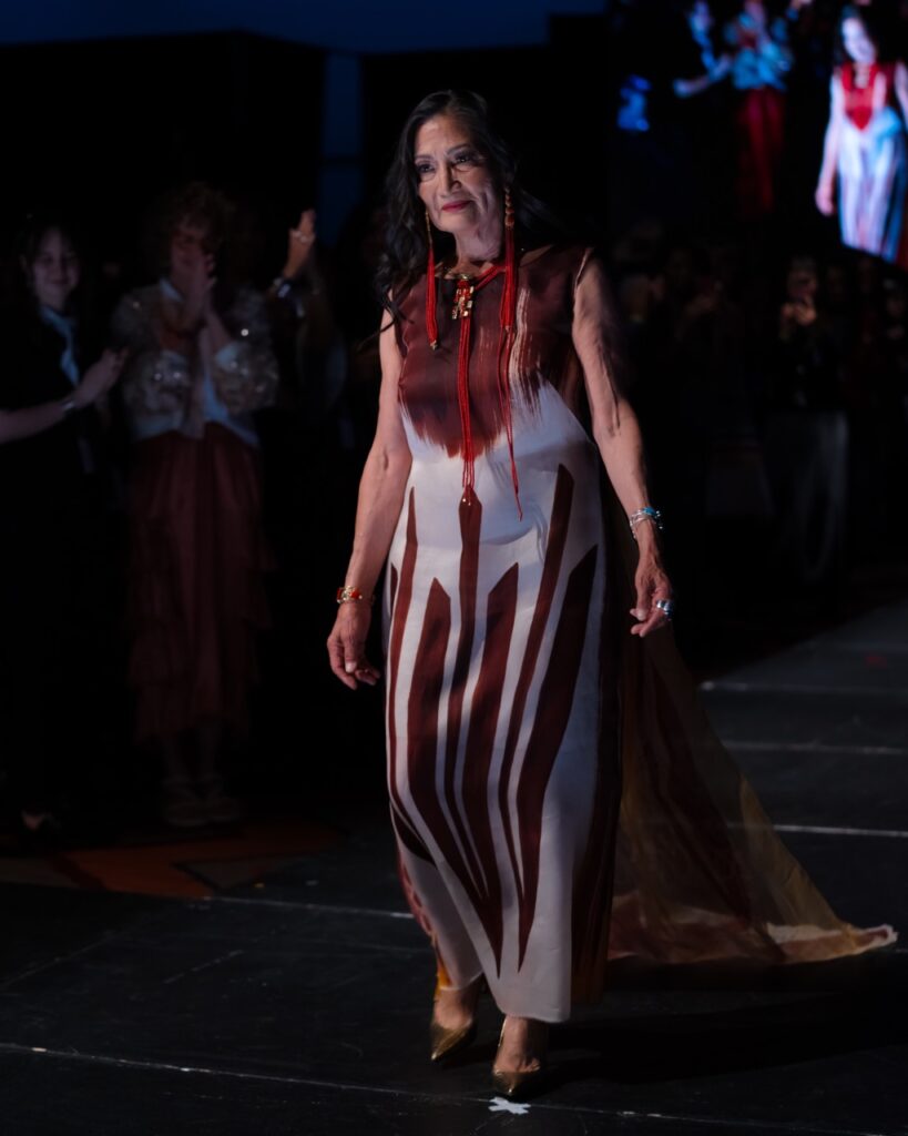 SWAIA Native Fashion Week TABLE Magazine A woman in a red and white dress walks down a runway.